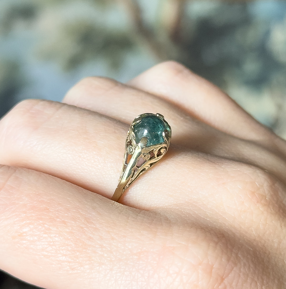 Side-on view showing the ring shown on a finger in profile, the cabochon raised on a tall gallery whose scrolled openwork shoulders curve down to the slim band.