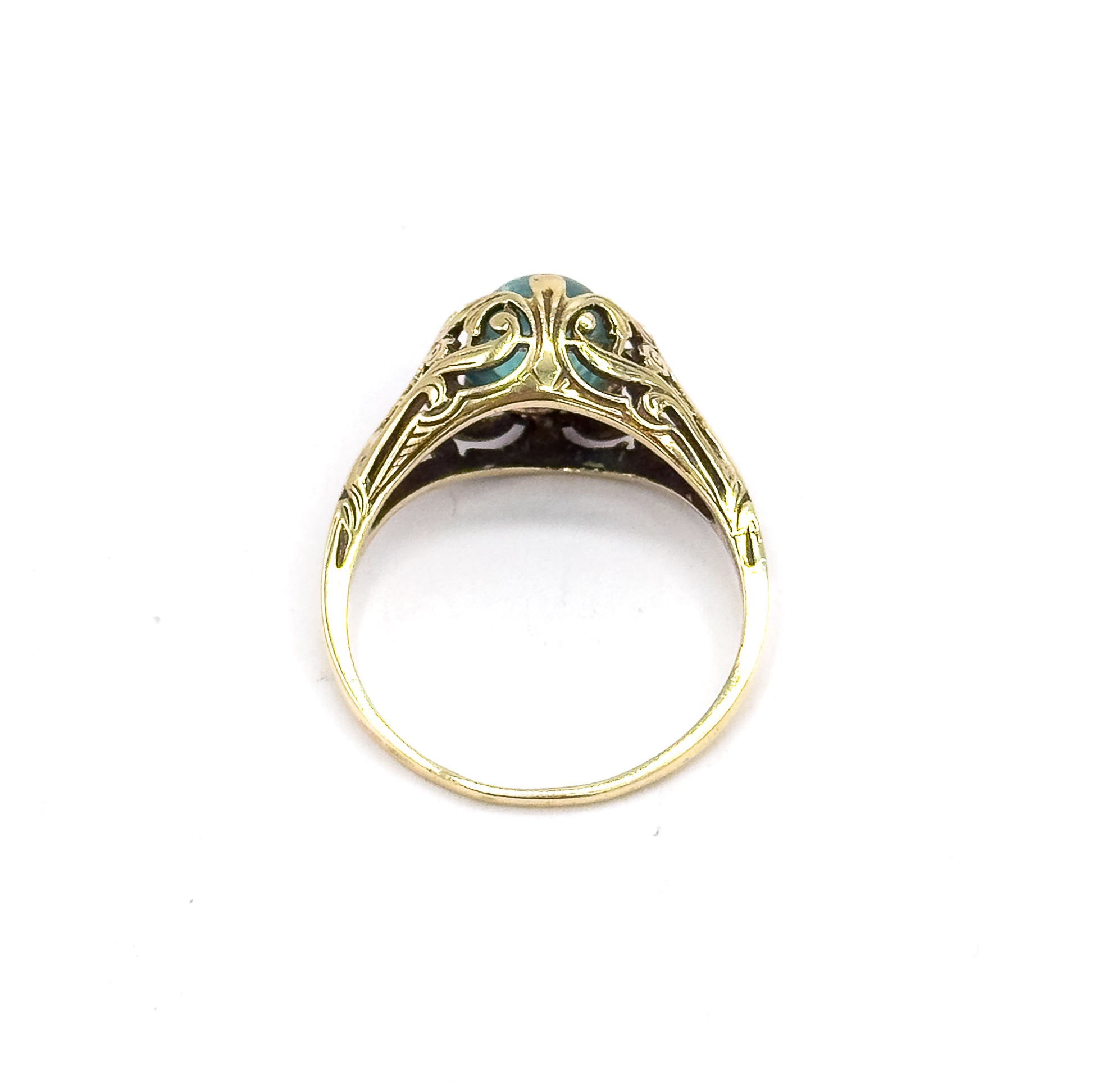 Head-on view standing upright against white, looking straight through the open circle of the shank to the scrolled pierced gallery, with just an edge of the greenish blue cabochon visible at the top.