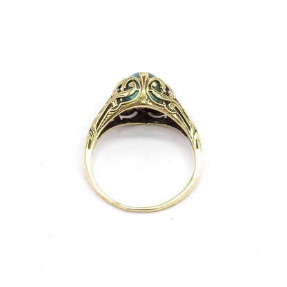 Head-on view standing upright against white, looking straight through the open circle of the shank to the scrolled pierced gallery, with just an edge of the greenish blue cabochon visible at the top.