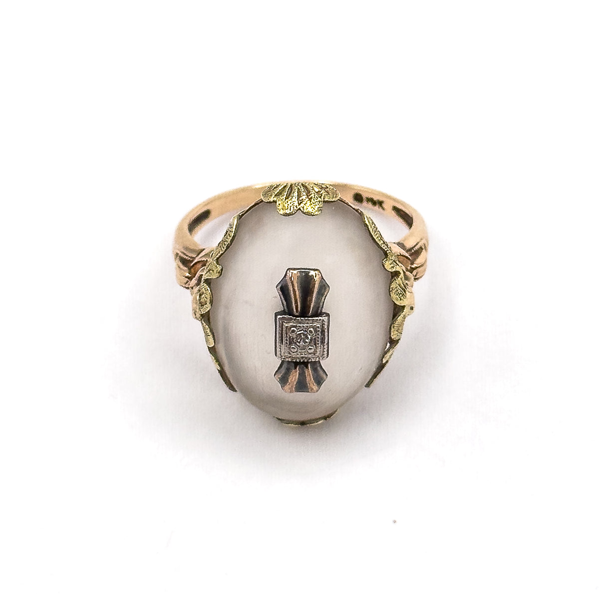 Face-on from above with the ring standing upright, showing the full oval cabochon, the central white metal plaque with its diamond, and leafy galleries curving down both sides to the shank.