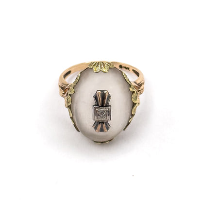Face-on from above with the ring standing upright, showing the full oval cabochon, the central white metal plaque with its diamond, and leafy galleries curving down both sides to the shank.
