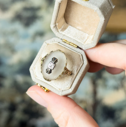 Retro rock crystal and diamond ring in 10K tritone gold, shown in a pale open ring box held between finger and thumb, the domed cabochon with its central diamond facing the camera.