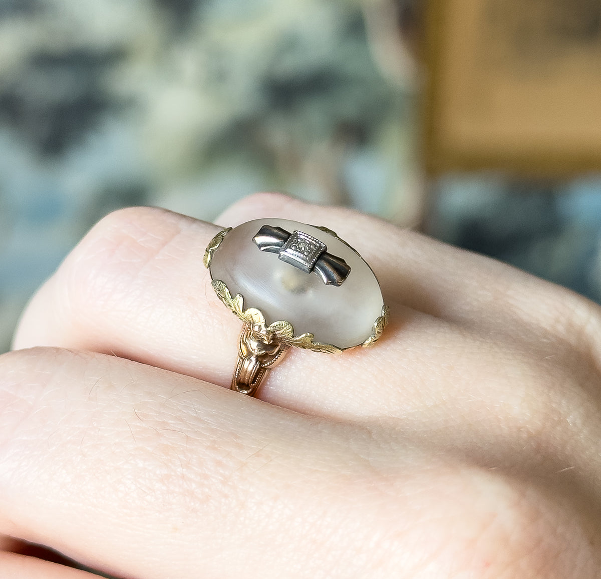 Shown on a finger in close-up, the domed rock crystal standing high above the knuckle with leafy tritone gold scrolls curving down the sides to the shank.