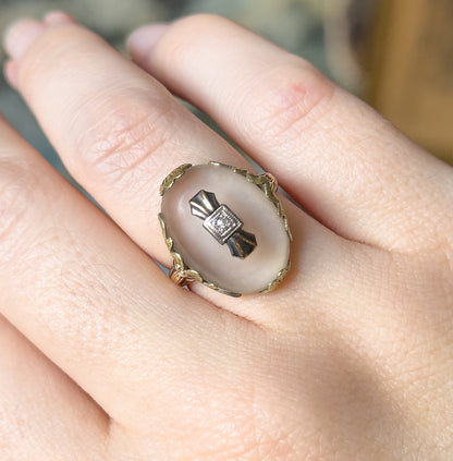 Shown on a finger from above with the hand tilted, so the oval face fills the finger width and the small white-gold bow and diamond accent read clearly against the crystal.