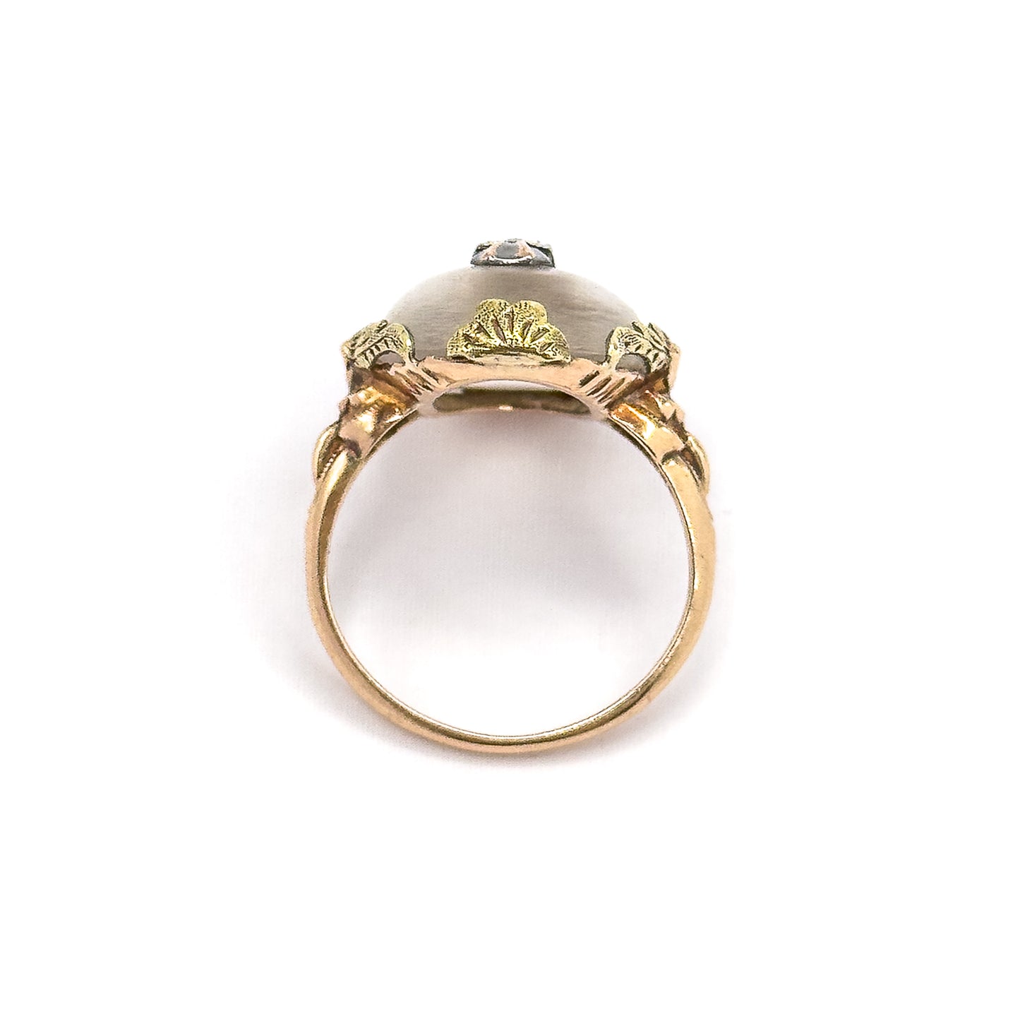 Viewed end-on through the open circle of the shank, showing the underside of the domed cabochon framed by three fan-shaped gold leaves and the diamond accent peeking over the top.