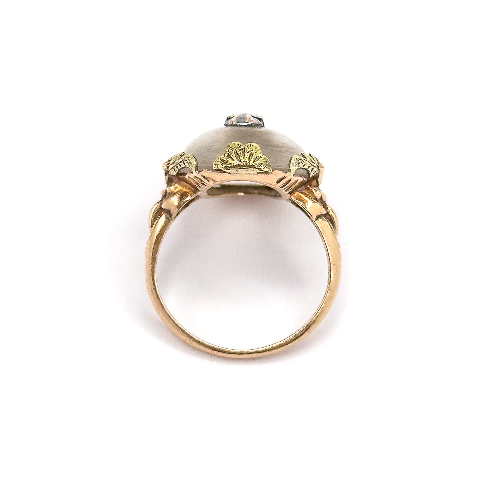 Viewed end-on through the open circle of the shank, showing the underside of the domed cabochon framed by three fan-shaped gold leaves and the diamond accent peeking over the top.