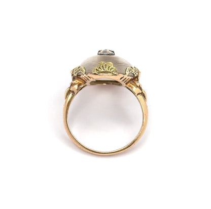 Viewed end-on through the open circle of the shank, showing the underside of the domed cabochon framed by three fan-shaped gold leaves and the diamond accent peeking over the top.
