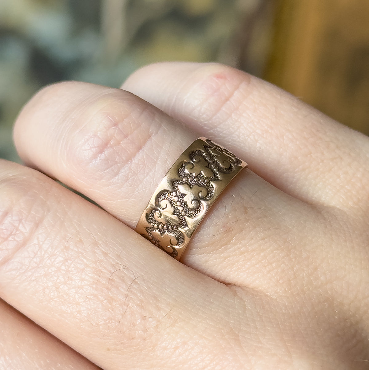 A Victorian rose gold heart band ring, shown on a finger, its wide band filled with raised scrolling heart motifs and beaded texture across the front of the shank.