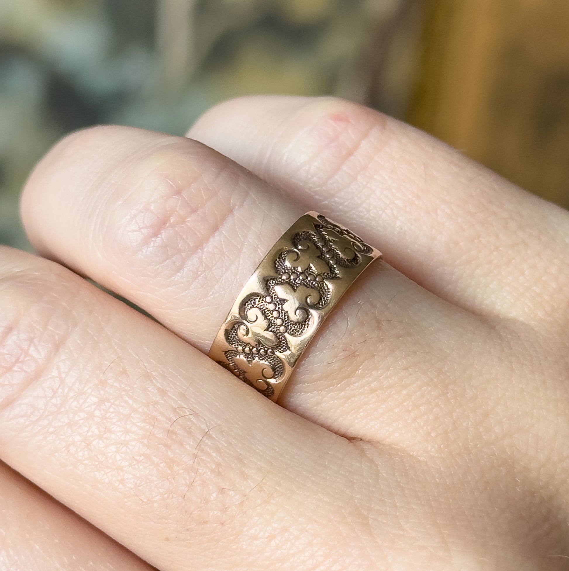 A Victorian rose gold heart band ring, shown on a finger, its wide band filled with raised scrolling heart motifs and beaded texture across the front of the shank.