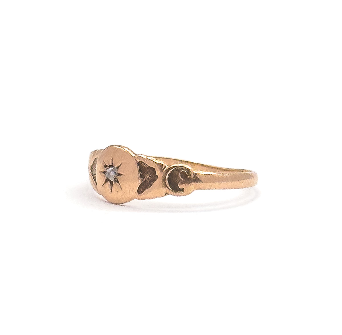 Close side view from the other flank, the star-set diamond catching light at the centre of the face with darkened engraved recesses and a scrolled curl at the shoulder beside the tapering shank.