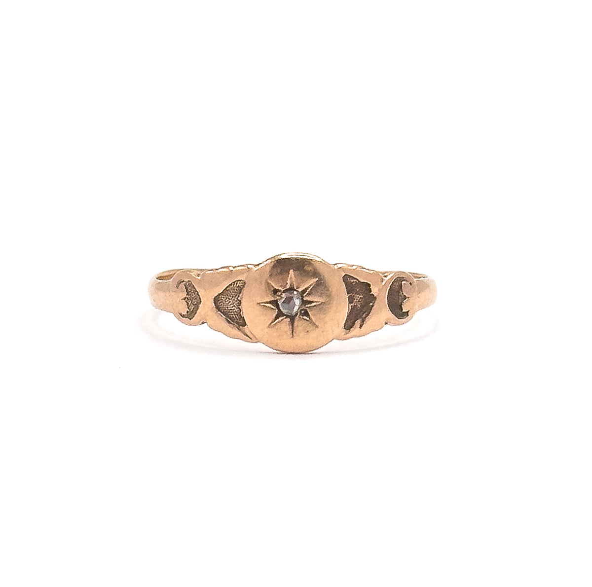 Head-on view with the whole ring small in the white frame, showing its tiny overall scale, the rose cut diamond bright in the star, scroll motifs at each shoulder and the shank slimming behind.