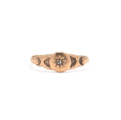 Head-on view with the whole ring small in the white frame, showing its tiny overall scale, the rose cut diamond bright in the star, scroll motifs at each shoulder and the shank slimming behind.