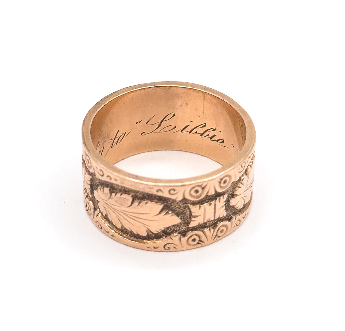 Seen from a low front angle, the deeply engraved leaf panel and its beaded scroll borders fill the outer band while the script inside the shank curves across the back wall above.