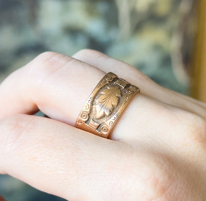 Victorian engraved leaf cigar band ring in 14K rose gold, shown on a finger, its wide band filled with a leaf motif and scrolled corners that give a sense of its substantial width.