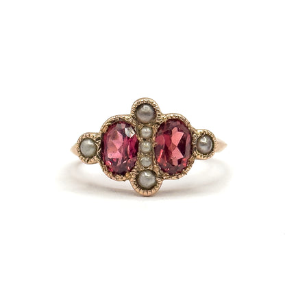 A close, tightly cropped face-on view filling the frame, showing the milled scalloped outline around the two pink garnets and the seven pearls, with the shank narrowing away at each side.