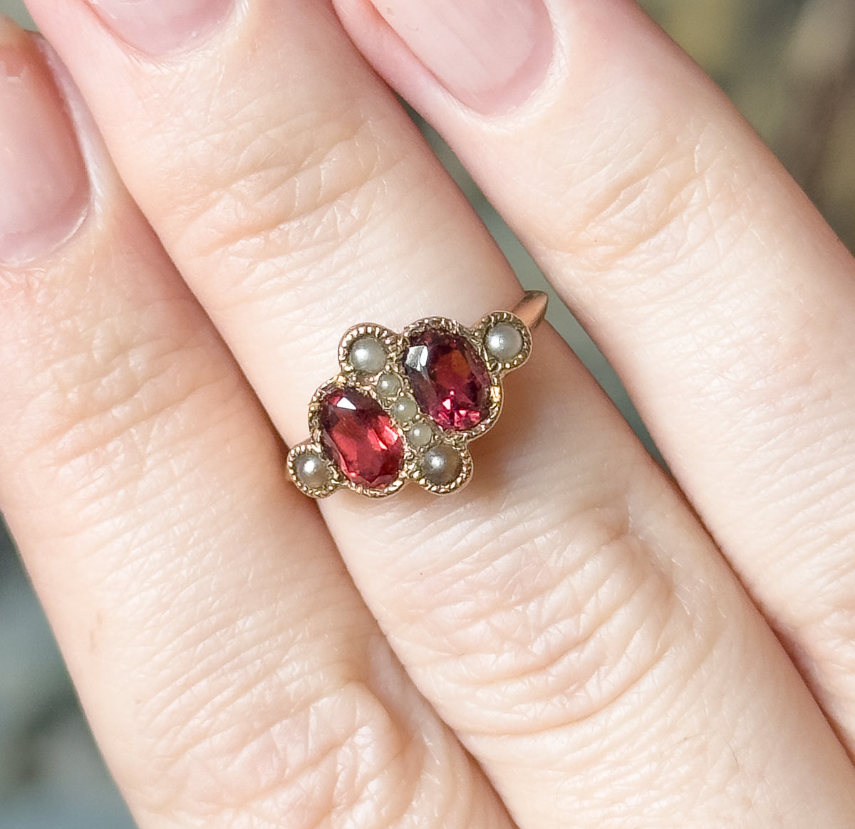 Shown on a finger from above, the beaded rose gold edging around each garnet bezel is visible, with the neighbouring fingers giving a sense of the ring's small scale.