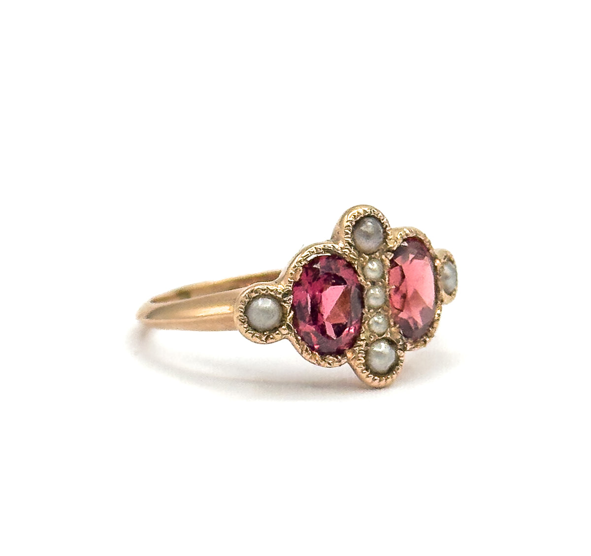 Standing upright against a plain white background, the ring is seen from the side so the low-set face, its three central seed pearls and the thin rose gold shank read clearly in profile.