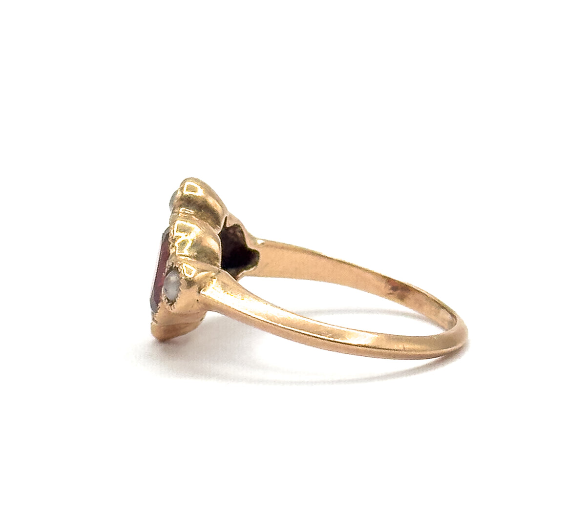 Seen edge-on from the opposite side, the shank sweeps up and flares into the shoulders, with the garnet showing as a slim pink line and the seed pearls in scalloped rose gold profile.