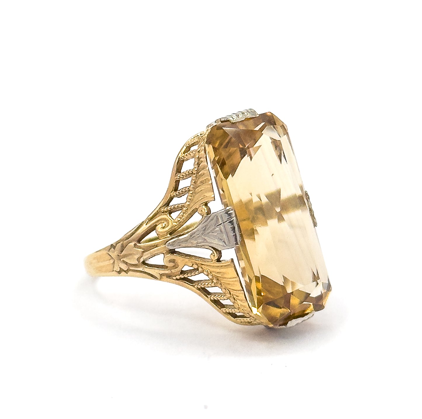 Upright side-on view with the citrine tilted toward the camera, its long stepped crown facets running the full height beside a white gold prong set midway along the pierced, milgrained gold shoulder.
