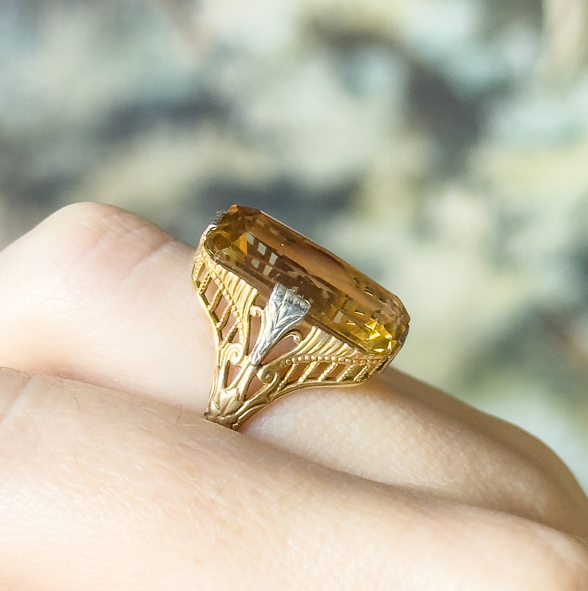 Side view shown on a finger, revealing the openwork filigree gallery, milgrain-edged scrollwork and a white gold prong rising to grip the citrine above the tapering shank.
