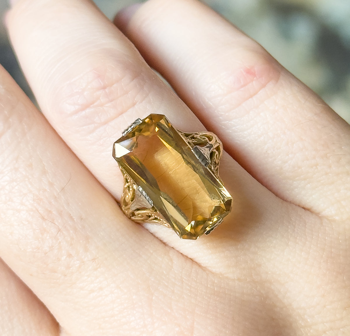 Close-up from directly above, shown on a finger, the citrine's flat table and stepped corner facets filling the frame between four white gold prongs, with the hand giving a sense of scale.