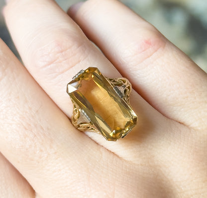 Close-up from directly above, shown on a finger, the citrine's flat table and stepped corner facets filling the frame between four white gold prongs, with the hand giving a sense of scale.