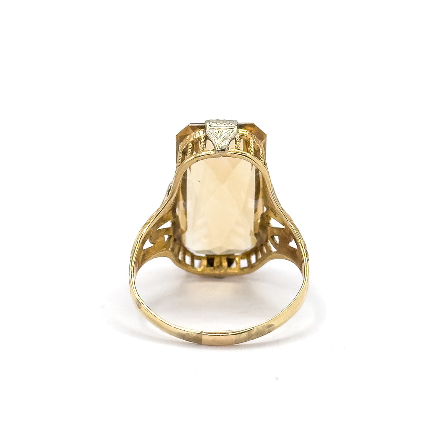 Reverse view off the hand, the shank standing upright so the citrine shows through the open back of the setting between pierced gallery bars and the scrolled openwork of the split shoulders.