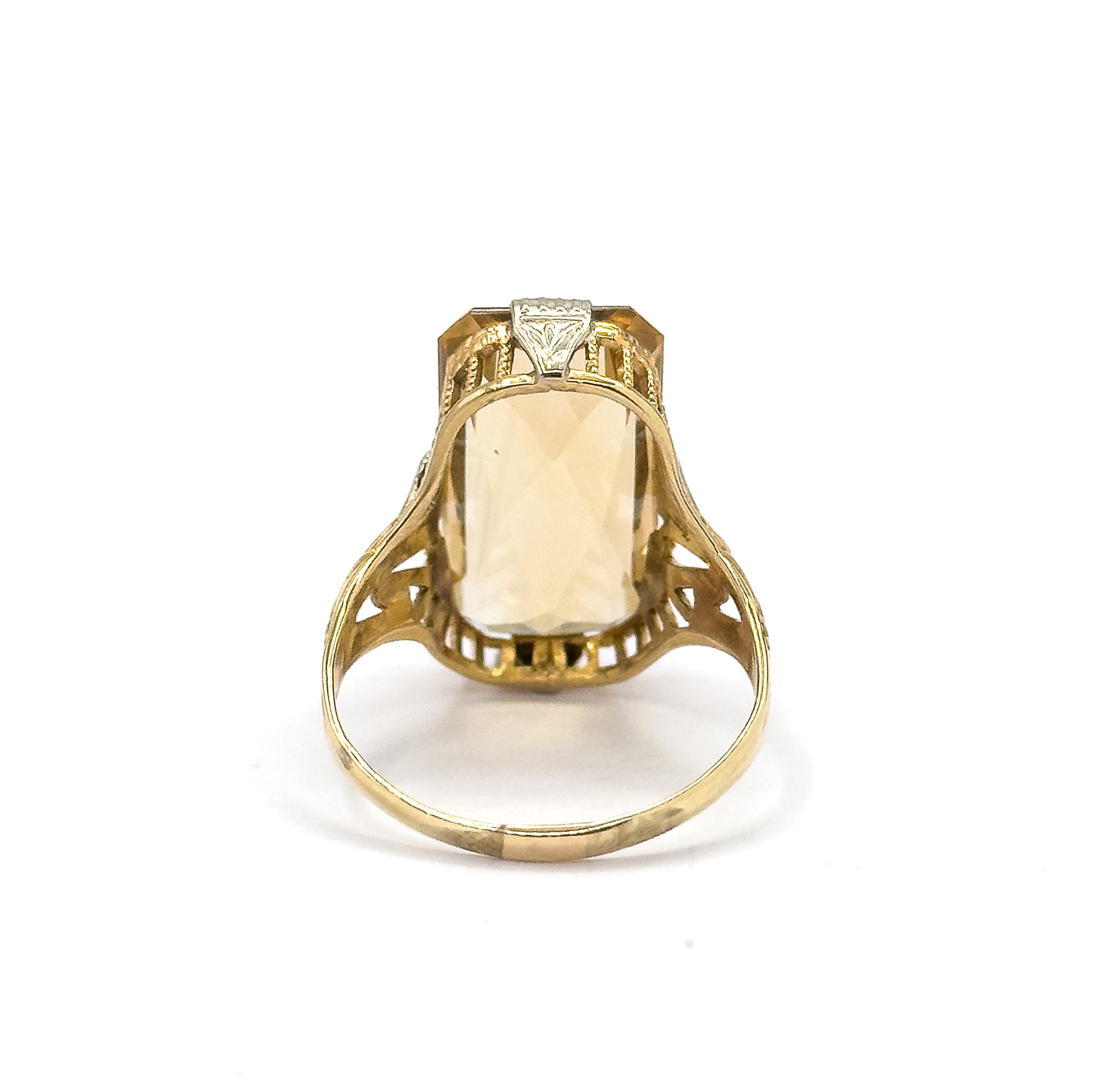 Reverse view off the hand, the shank standing upright so the citrine shows through the open back of the setting between pierced gallery bars and the scrolled openwork of the split shoulders.