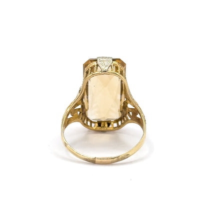 Reverse view off the hand, the shank standing upright so the citrine shows through the open back of the setting between pierced gallery bars and the scrolled openwork of the split shoulders.