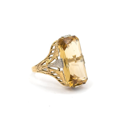 Angled three-quarter view against white, the elongated citrine tilted so its long side facets and a white gold side prong show above the scrolled, milgrained filigree shoulder.