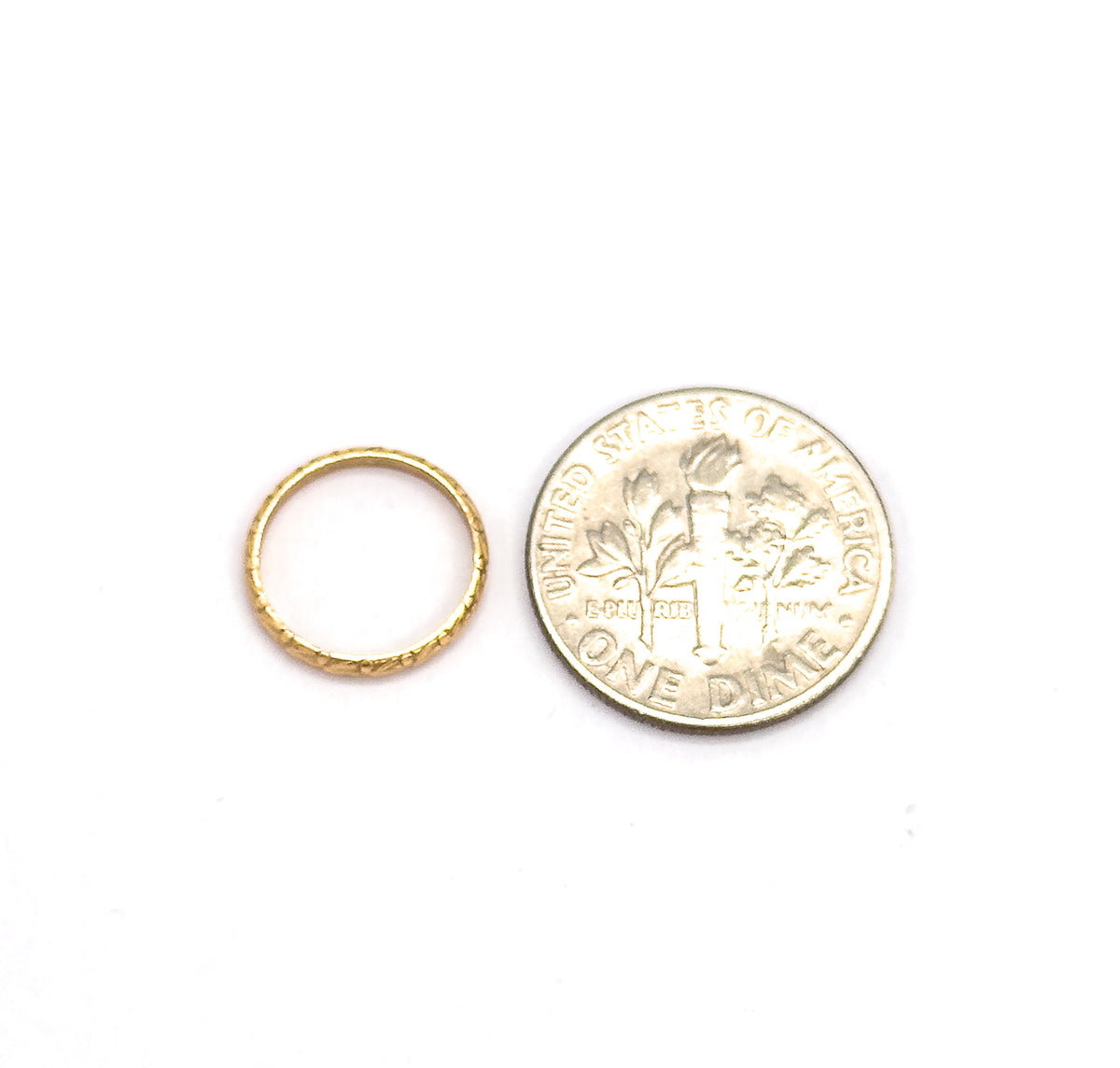 The ring lies flat beside a dime, its slender chased band barely over half the coin's width, giving a clear sense of scale.