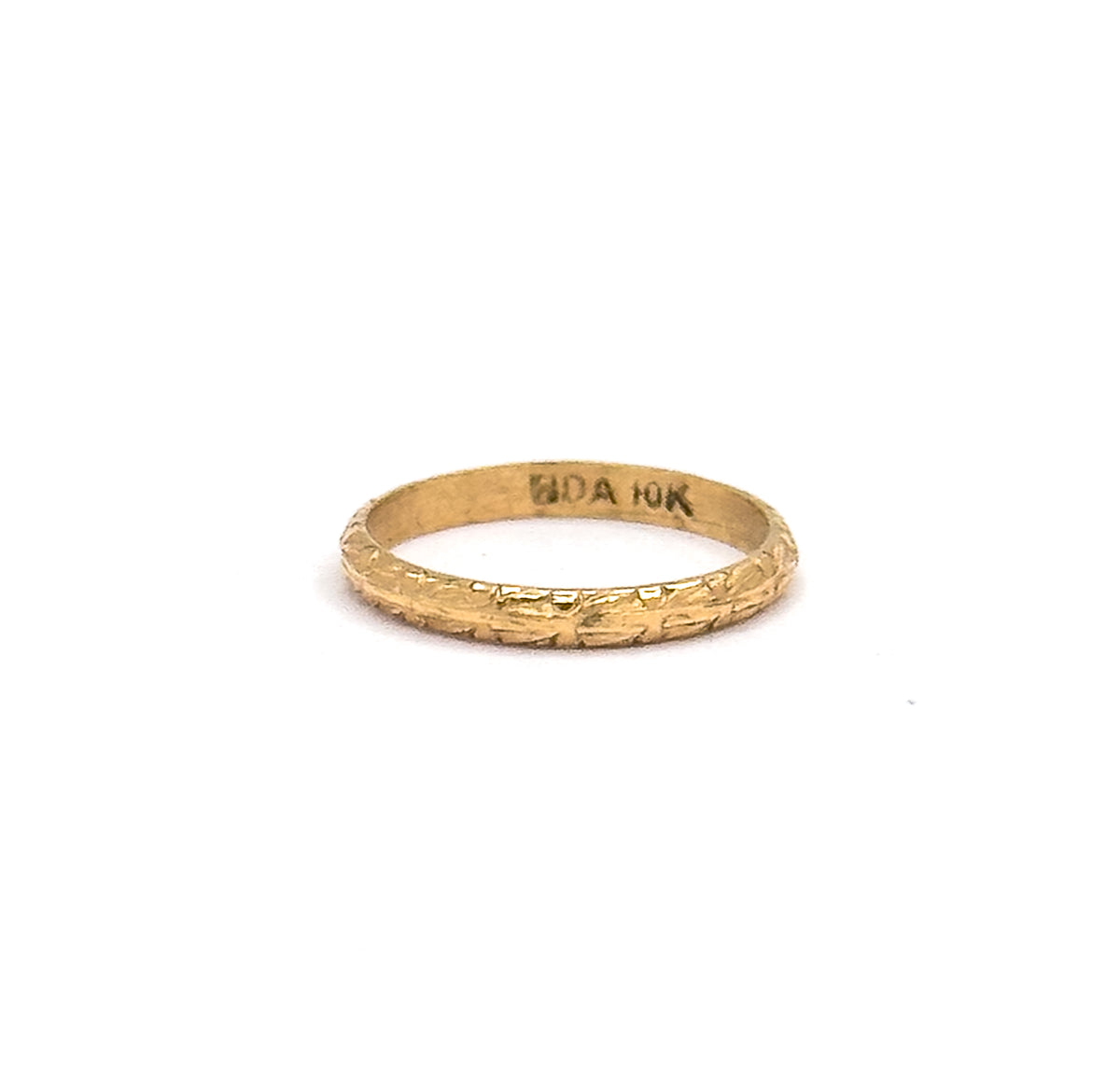 The ring stands upright on a white background, chased texture catching light along the front of the shank and a stamped mark visible inside the back of the band.