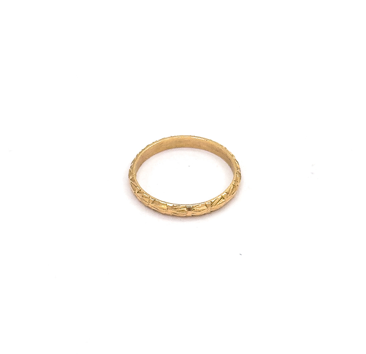 Angled from above and behind, the narrow yellow gold band appears as a flattened oval, chased cuts glinting along the far side while the inner wall curves away into shadow.