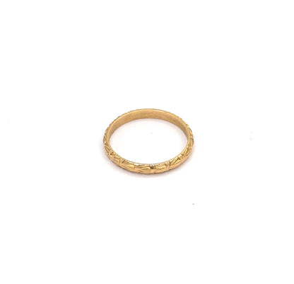 Angled from above and behind, the narrow yellow gold band appears as a flattened oval, chased cuts glinting along the far side while the inner wall curves away into shadow.