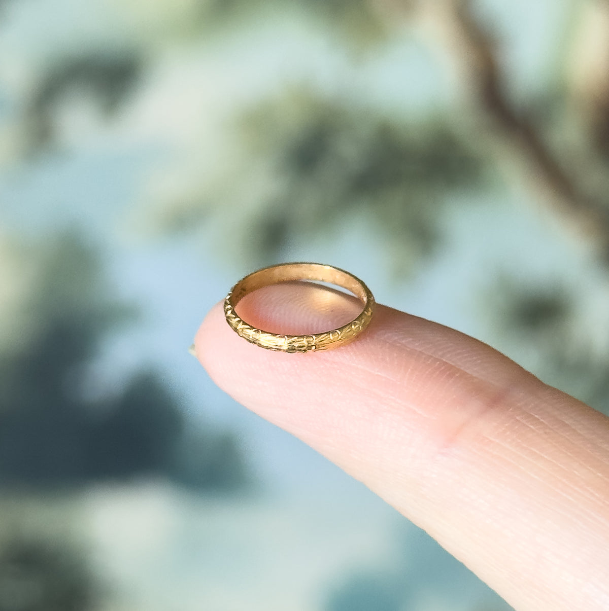 Edwardian chased baby ring in 10K yellow gold, shown balanced on a fingertip that makes clear how tiny it is, with chased detailing running around the narrow band.