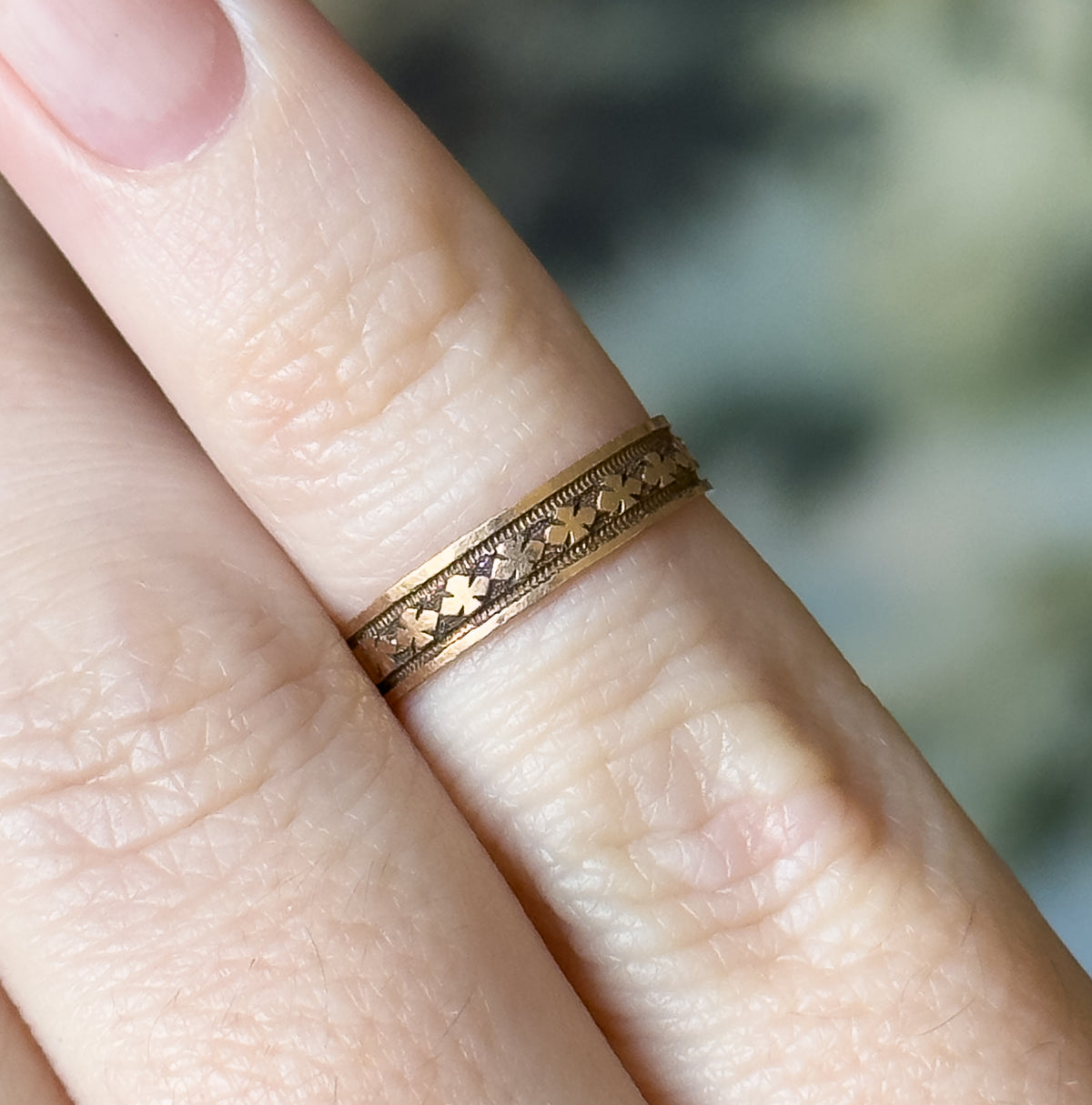 The band shown higher on the finger, its repeating clover motif running along the centre between beaded borders, dark patina settled in the recesses.