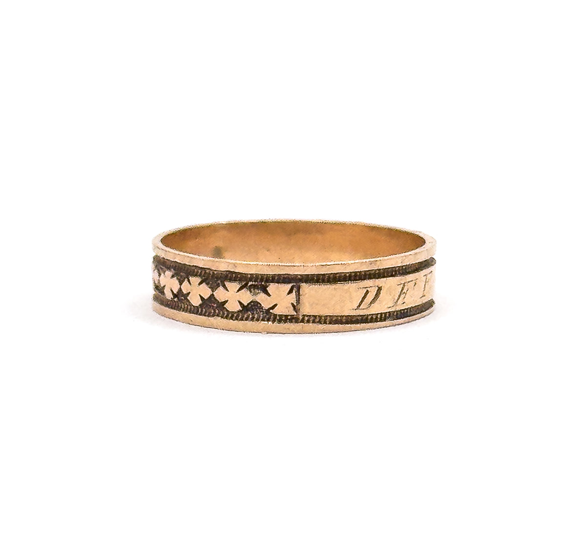 The ring stands upright against a white background, showing the whole hoop from the side with clover motifs at left and the engraved cartouche letters beginning at right.