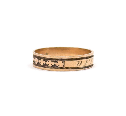 The ring stands upright against a white background, showing the whole hoop from the side with clover motifs at left and the engraved cartouche letters beginning at right.