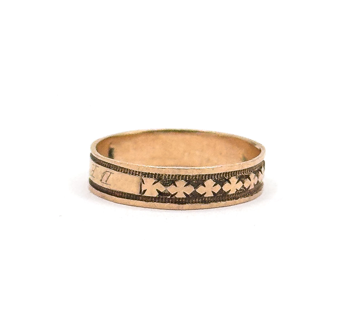 Upright against white and turned so the run of clover motifs fills the front of the band while the cartouche letters slip away at the left edge, the smooth inner shank visible above.