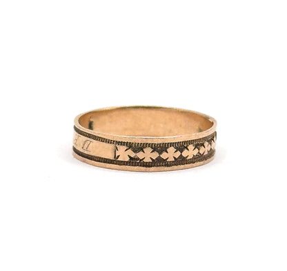 Upright against white and turned so the run of clover motifs fills the front of the band while the cartouche letters slip away at the left edge, the smooth inner shank visible above.