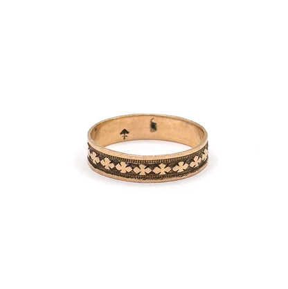 Shown small within a wide field of white, conveying how petite the band is, with the anchor stamp inside the shank and the clover row running along the front.