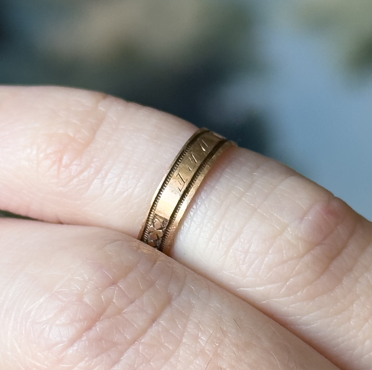 Victorian engraved clover band in 9K rose gold, shown close up on a finger, the narrow shank's beaded edges and engraved cartouche of initials catching the light against the skin.