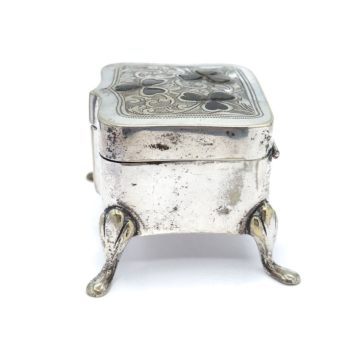 End view from the narrow short side, showing the box's depth, the seam where the lid meets the body, a small catch at the right edge, and two teardrop feet splaying forward.