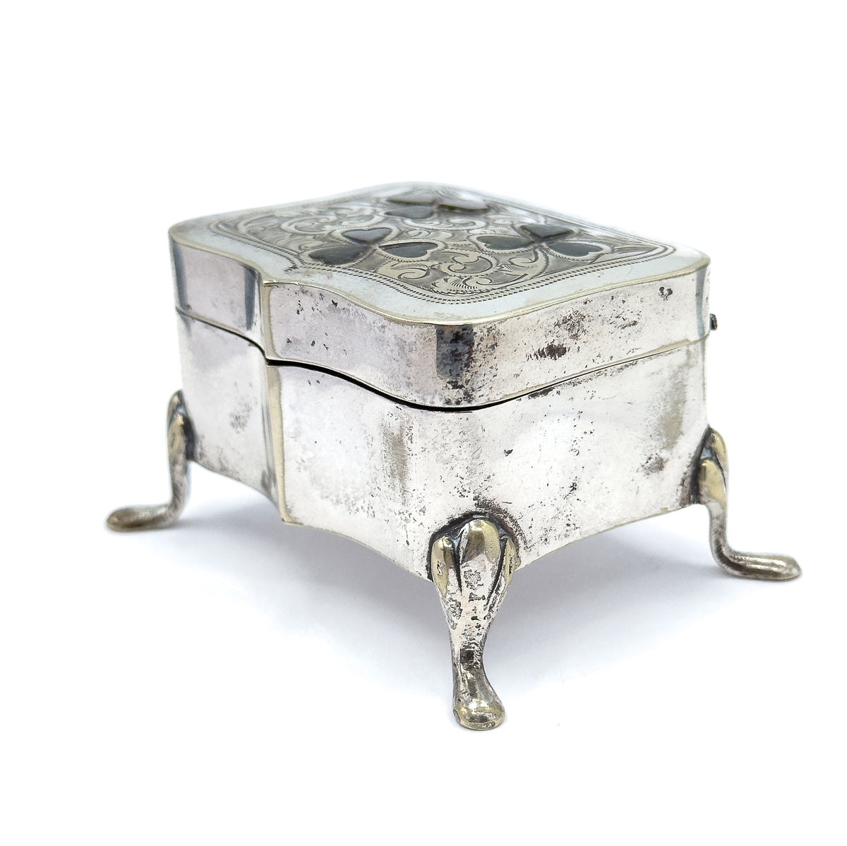 High three-quarter view from above, looking down onto the full engraved lid with its three green marble clovers, the serpentine body below and three teardrop feet splaying outward.