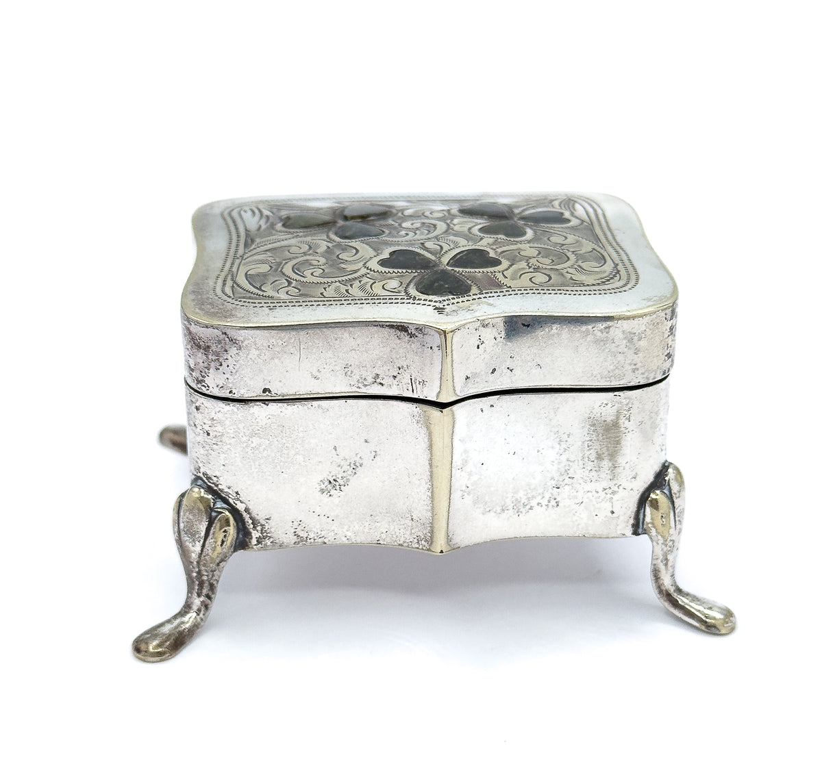 Near eye-level from the front, the shaped body filling the frame with its wavy seam and centre ridge, the engraved lid seen edge-on above and two front feet splaying wide below.