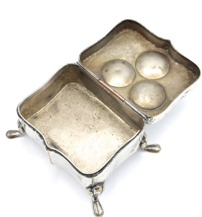 Angled overhead view into the open box, where three round domed bumps show through the inside of the lid behind the clovers, with the deep shaped body and its teardrop feet alongside.