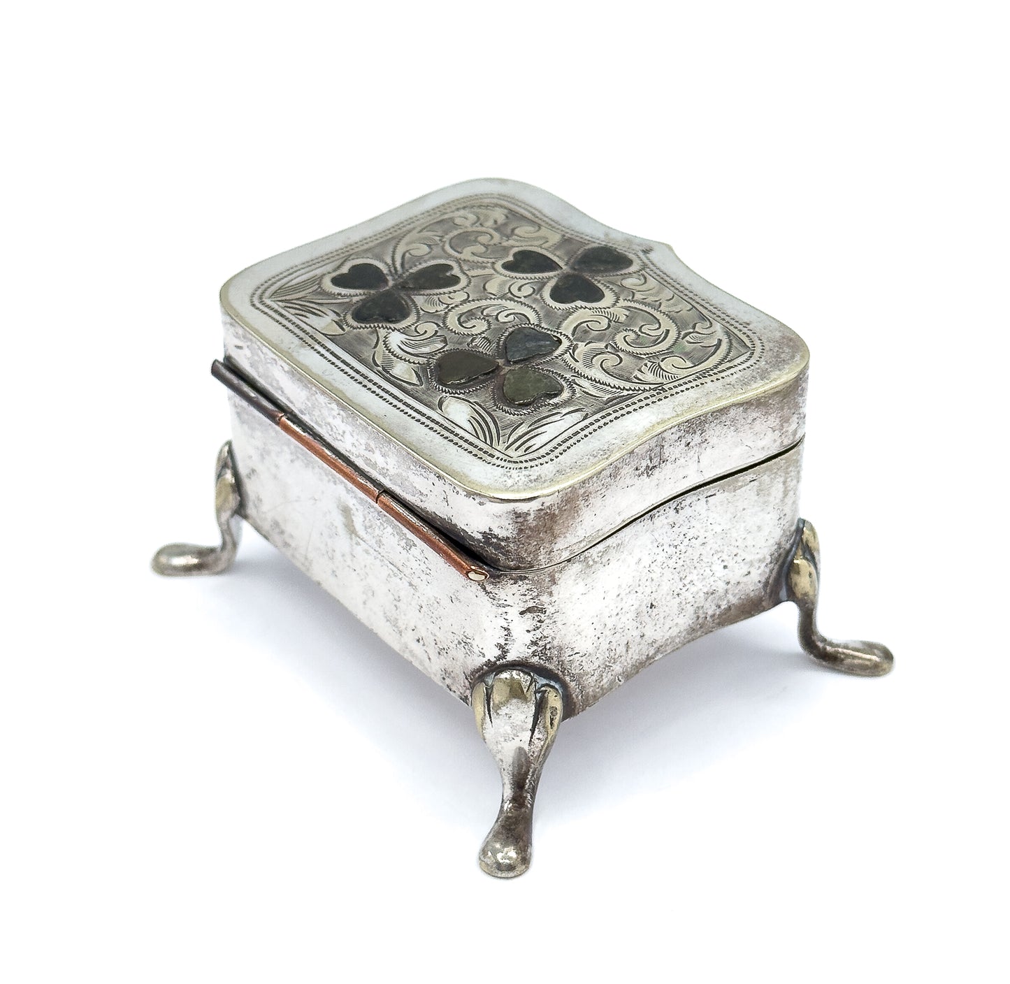 Lower three-quarter view from the hinged back edge, where the hinge barrel runs along the side, the plain engraved body sits deep above two splayed teardrop feet, and the shaped lid overhangs.