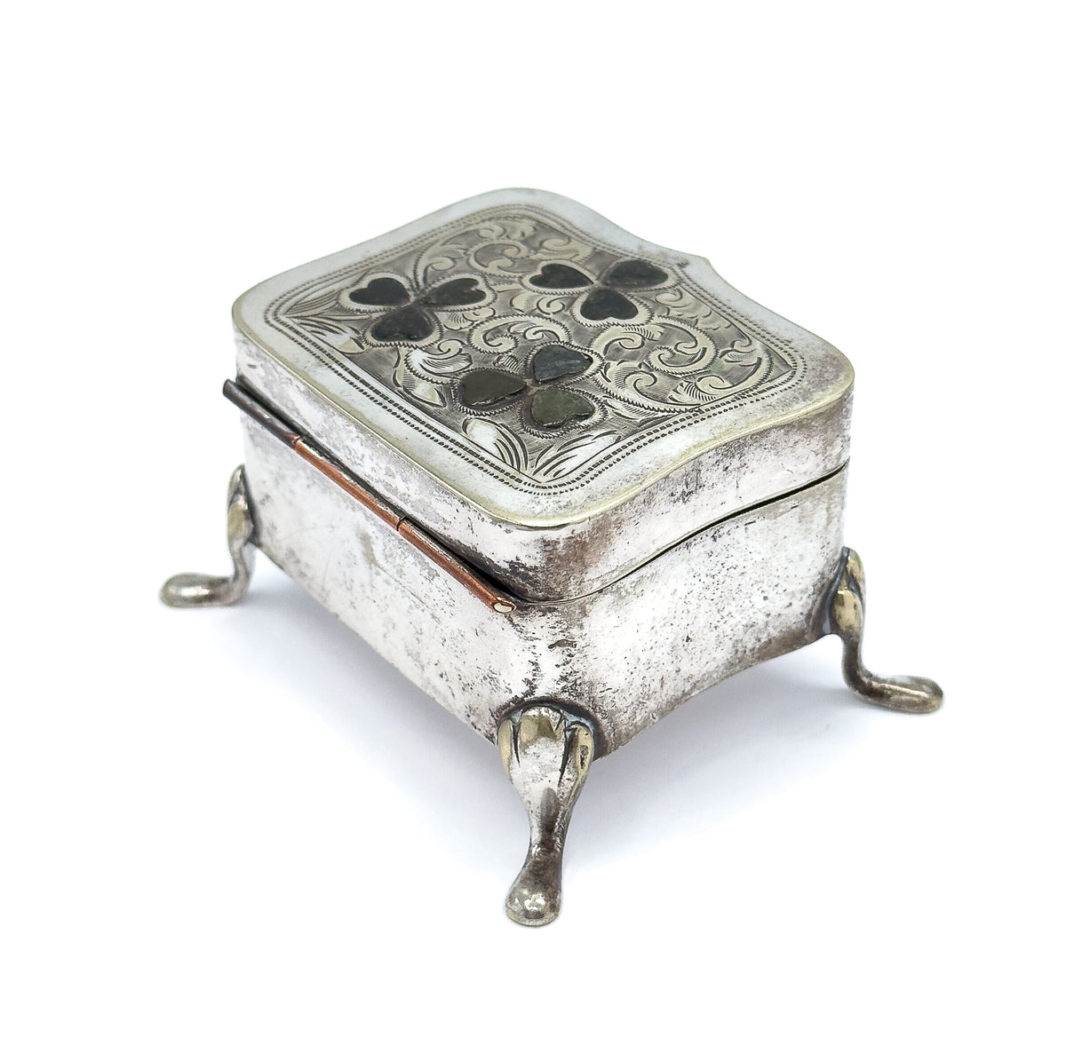 Lower three-quarter view from the hinged back edge, where the hinge barrel runs along the side, the plain engraved body sits deep above two splayed teardrop feet, and the shaped lid overhangs.