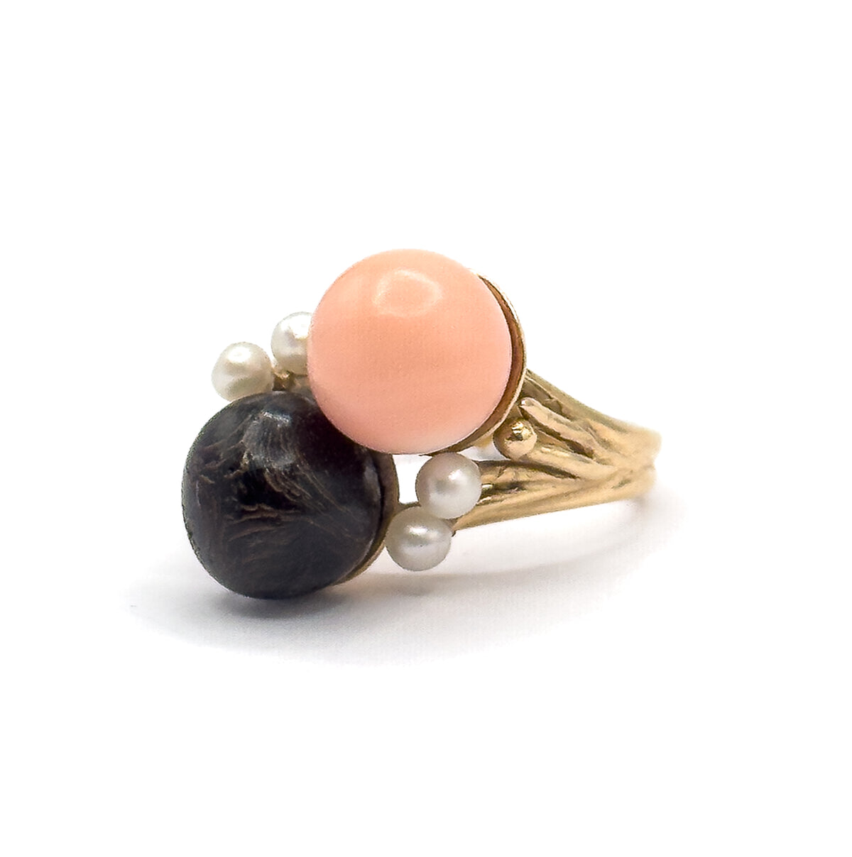 Side view from the pearl side, two seed pearls clustered above the peachy pink orb and two more below beside the dark textured orb, the yellow gold shank sweeping away to the right.