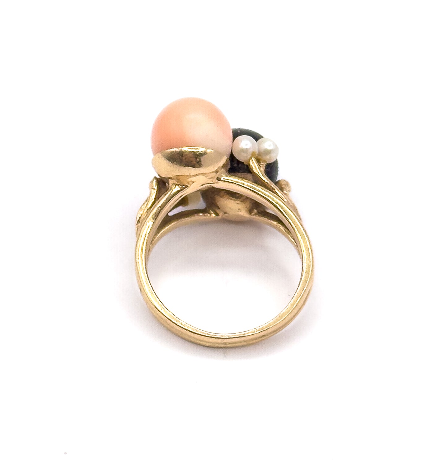 Upright rear view against white, looking through the open round shank to the yellow gold cup beneath the peachy pink orb, with two seed pearls and the dark coral orb behind.